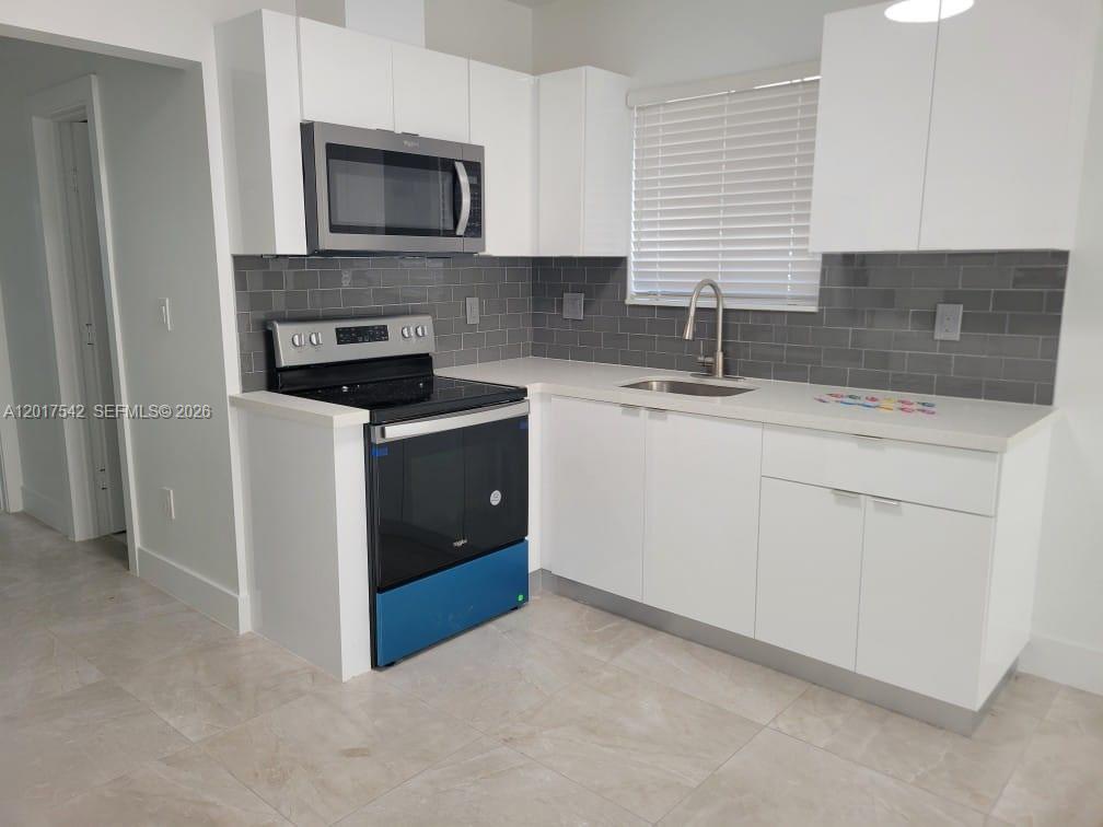 A kitchen features white cabinets, a stainless steel microwave, a black stove, and gray backsplash — 1725 Calais Dr # 6, Miami Beach FL 33141, MIAMI BEACH, FL