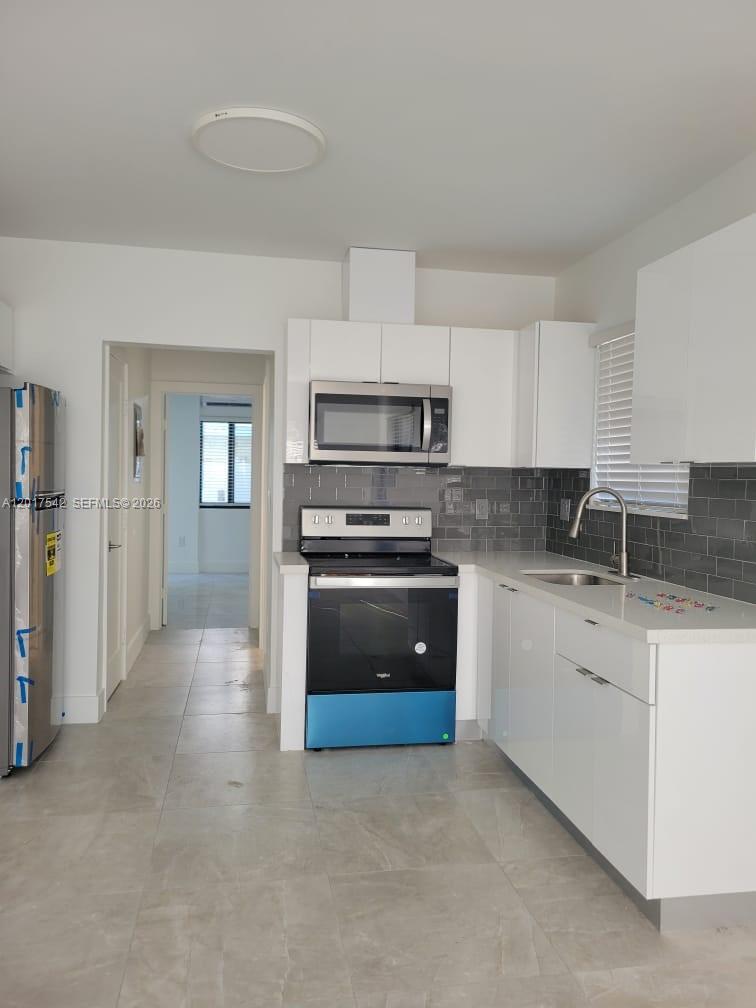 A modern kitchen features white cabinets, stainless steel appliances, and gray subway tile backsplashes — 1725 Calais Dr # 6, Miami Beach FL 33141, MIAMI BEACH, FL