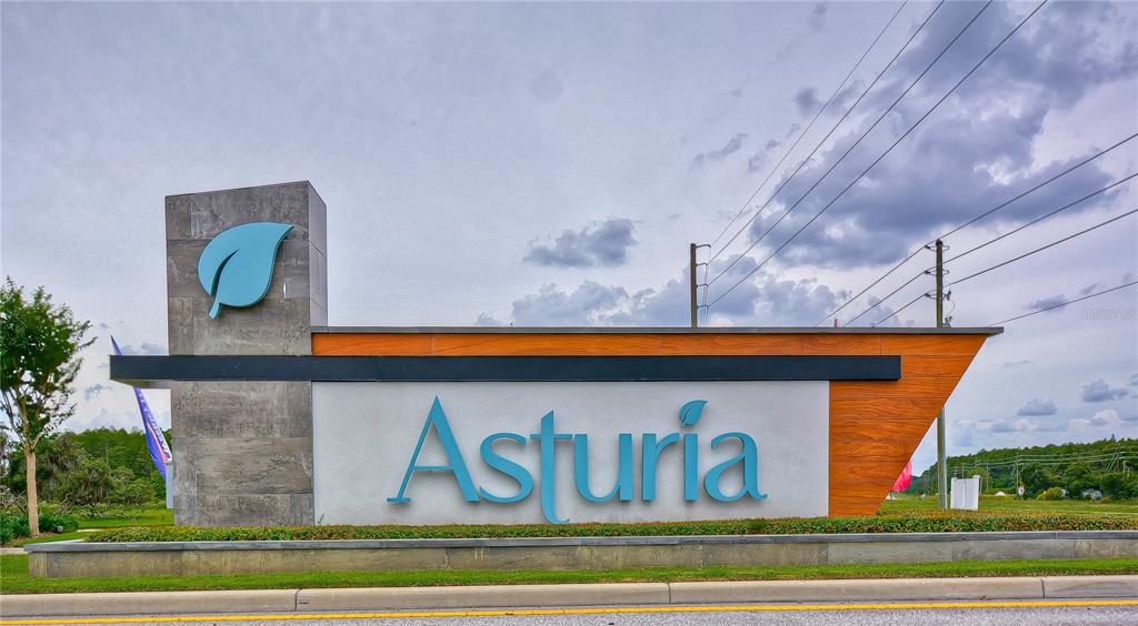 A modern monument sign for the Asturia community features a large blue leaf logo — 15371 CARAVAN AVENUE, ODESSA, FL