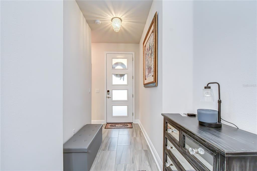 A bright entryway features a white front door, a gray storage bench, and a dresser — 15371 CARAVAN AVENUE, ODESSA, FL