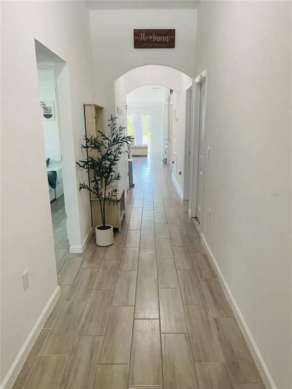 A long hallway with light wood-look tile flooring leads toward an arched entryway — 1409 HILLSBOROUGH WAY, KISSIMMEE, FL
