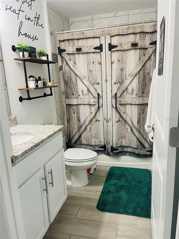 A bathroom features a vanity with a granite countertop, a toilet, and a barn-door shower curtain — 1409 HILLSBOROUGH WAY, KISSIMMEE, FL
