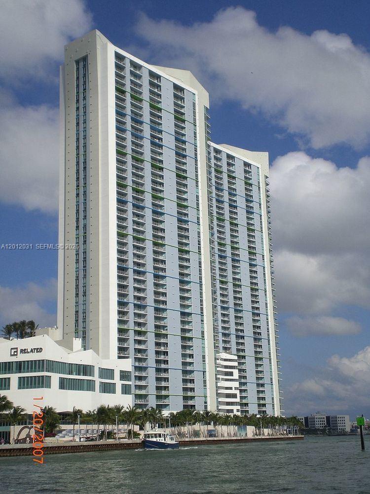 A tall, modern residential high-rise building stands along a waterfront with palm trees — 335 S Biscayne Blvd # 2900, Miami FL 33131, MIAMI, FL