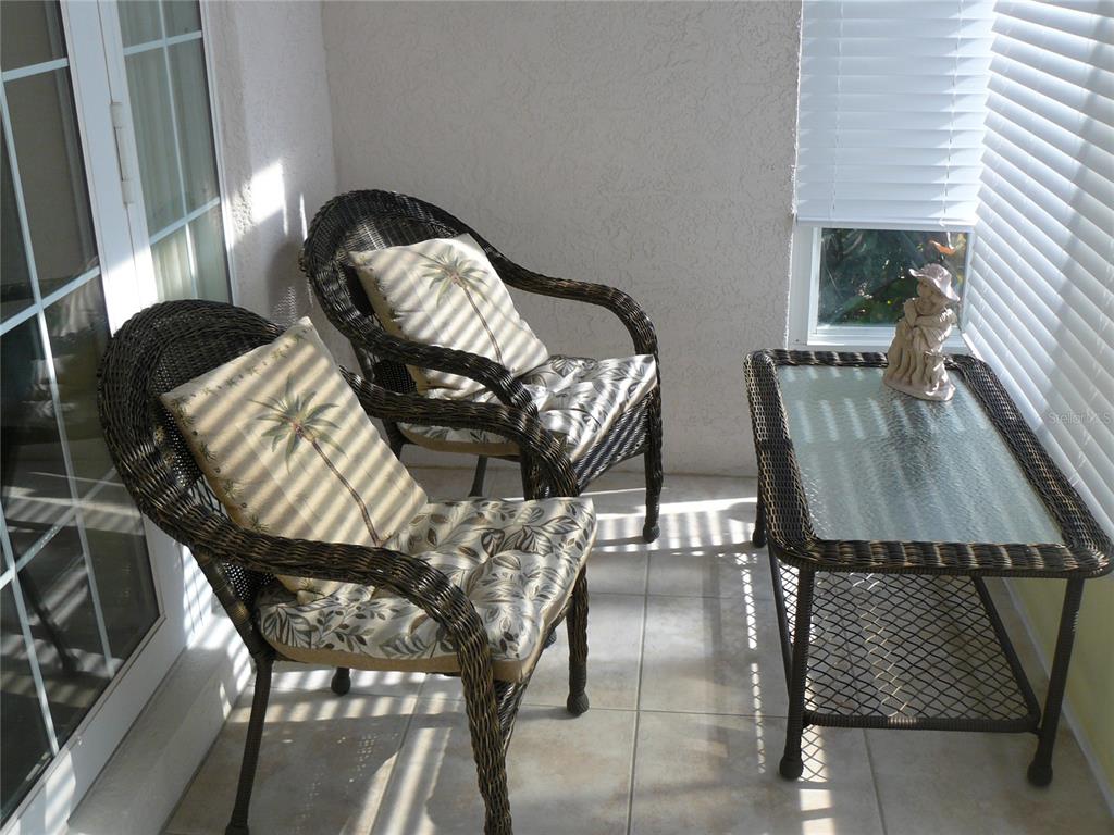 A sunroom features two wicker chairs with palm-print cushions and a matching glass-top table — 8628 SWEET MAGNOLIA PLACE, SEMINOLE, FL