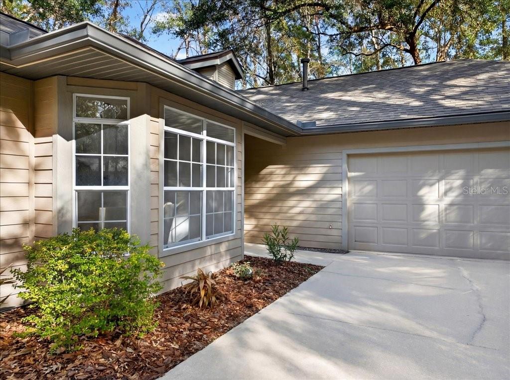 A tan house exterior features a concrete driveway, a garage, and a landscaped front yard — 4412 SW 101ST DRIVE, GAINESVILLE, FL