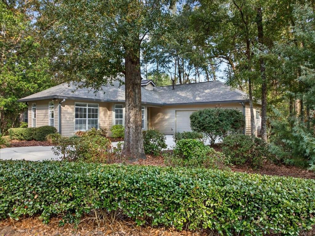 A single-story house with tan siding and a two-car garage sits behind a large hedge — 4412 SW 101ST DRIVE, GAINESVILLE, FL