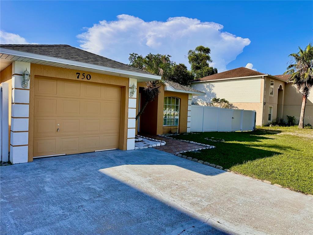 A single-story house with a tan stucco exterior, a garage, and a white privacy fence — 750 PELICAN COURT, KISSIMMEE, FL