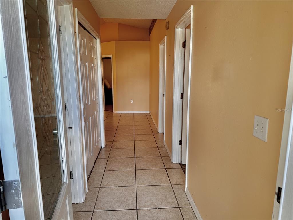 A hallway with tan walls and light-colored tile flooring leads toward a doorway — 750 PELICAN COURT, KISSIMMEE, FL