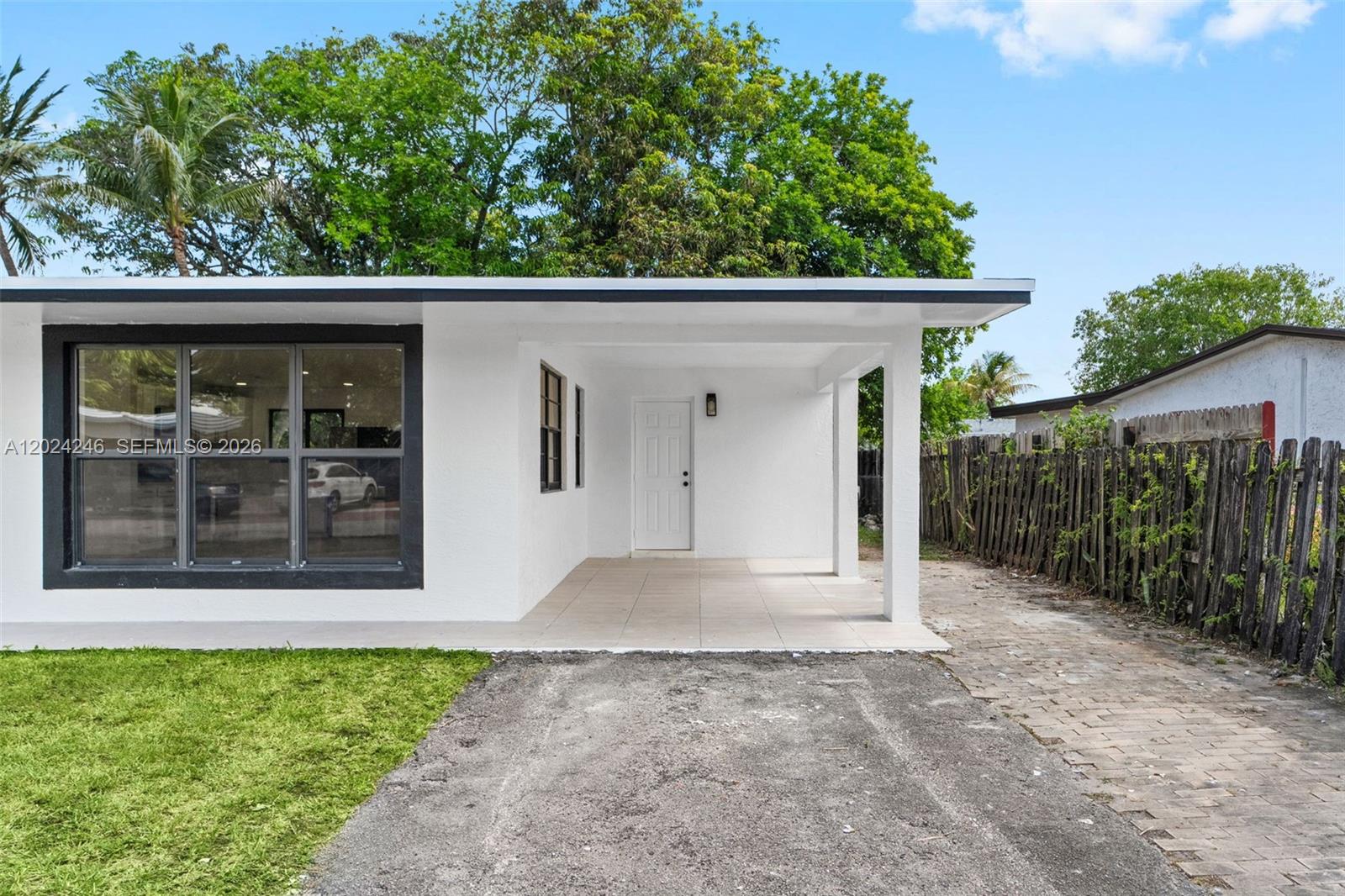 The exterior of a white house features a covered porch, a large window, and driveway — 4830 NW 13th St, Lauderhill FL 33313, LAUDERHILL, FL