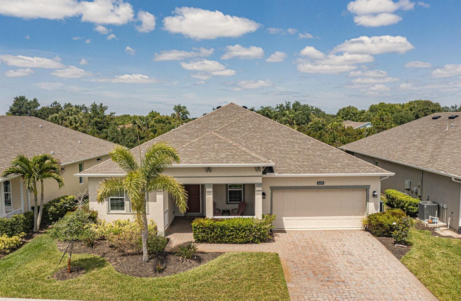 An aerial view shows a single-story house with a tan exterior, shingle roof, and brick driveway — 3409 Wild Banyan Way, Vero Beach FL 32966, VERO BEACH, FL