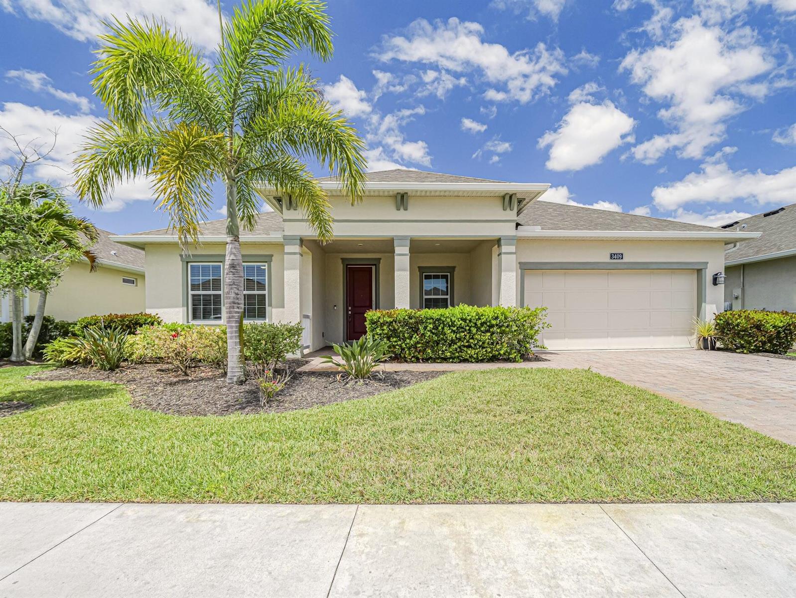 A single-story house with a palm tree, a two-car garage, and a red front door — 3409 Wild Banyan Way, Vero Beach FL 32966, VERO BEACH, FL