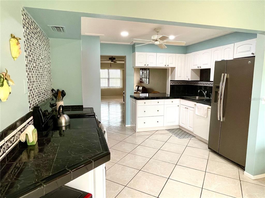 A kitchen features white cabinets, black countertops, a stainless steel refrigerator, and light-colored tile flooring — 305 30TH AVENUE W UNIT A307, BRADENTON, FL