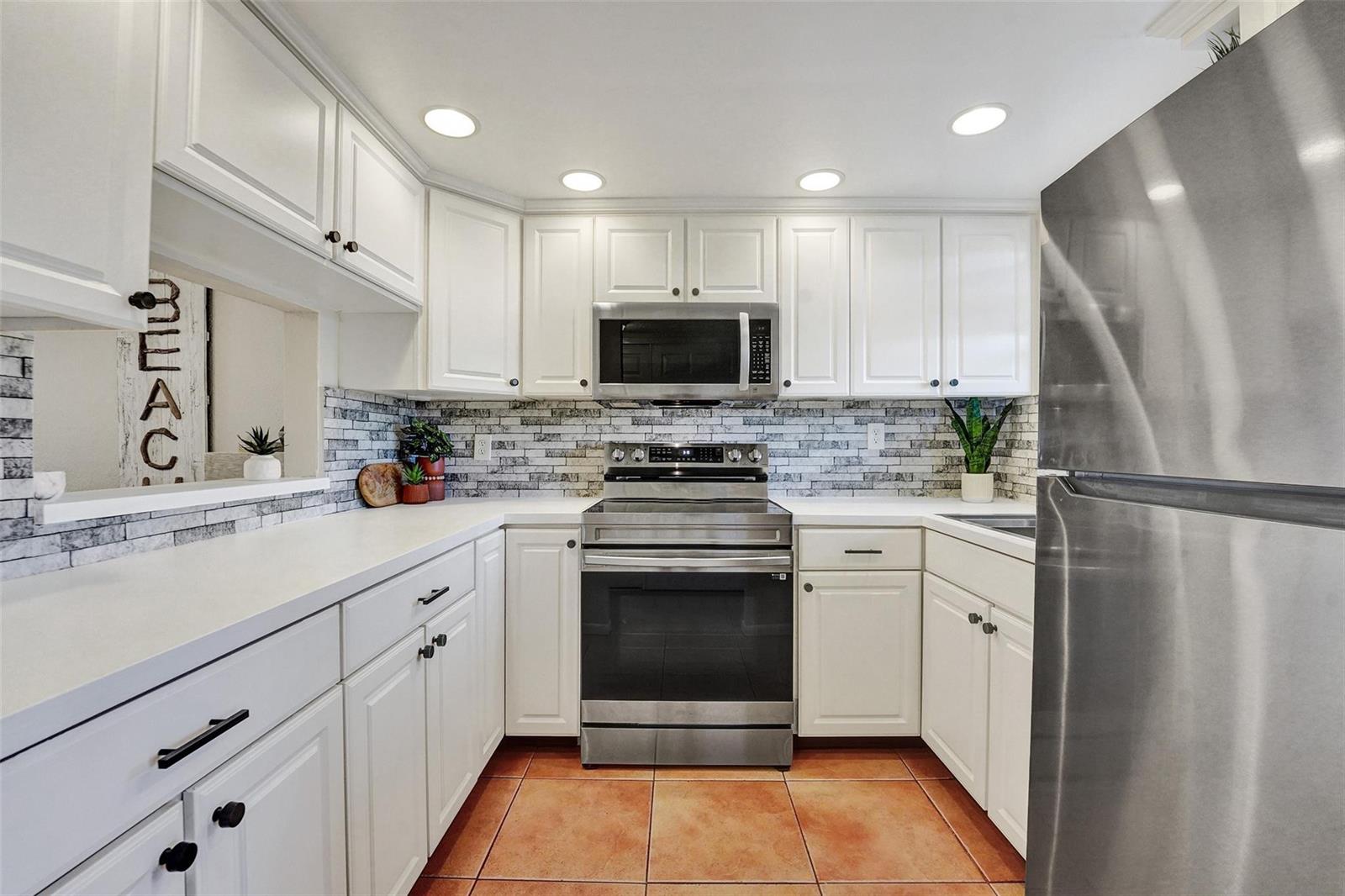 A kitchen features white cabinetry, stainless steel appliances, a tiled backsplash, and terracotta floor tiles — 6570 Royal Palm Boulevard # 210j, Margate FL 33063, MARGATE, FL