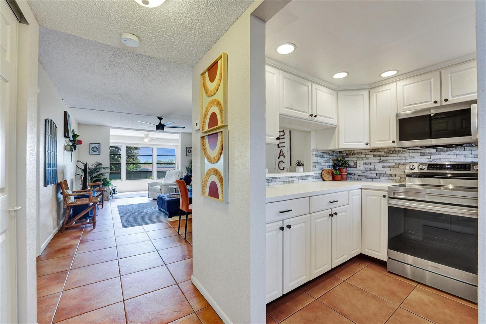 A kitchen with white cabinets and stainless steel appliances opens into a tiled living area — 6570 Royal Palm Boulevard # 210j, Margate FL 33063, MARGATE, FL