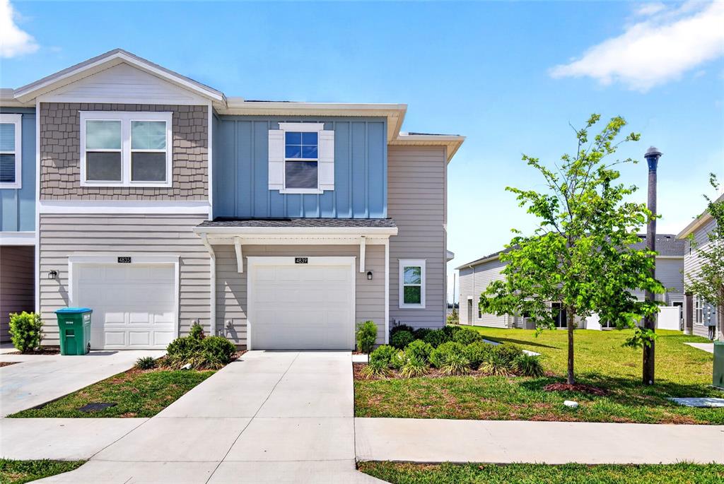 A two-story townhouse with a blue and gray exterior, white garage doors, and a lawn — 4839 SW 81ST LOOP, OCALA, FL