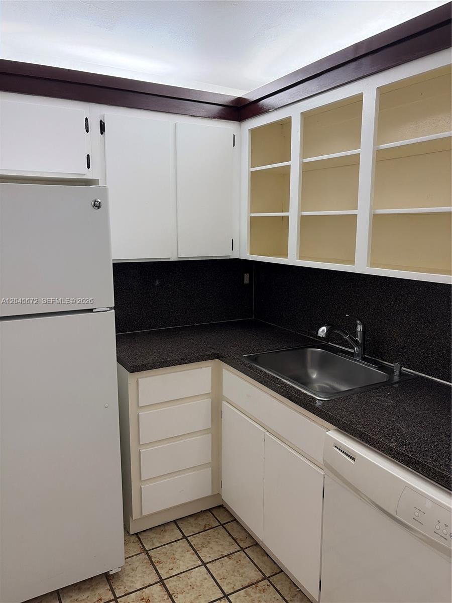 A kitchen features white cabinets, dark countertops, a stainless steel sink, and a white refrigerator — 1150 Collins Ave # 404, Miami Beach FL 33139, MIAMI BEACH, FL