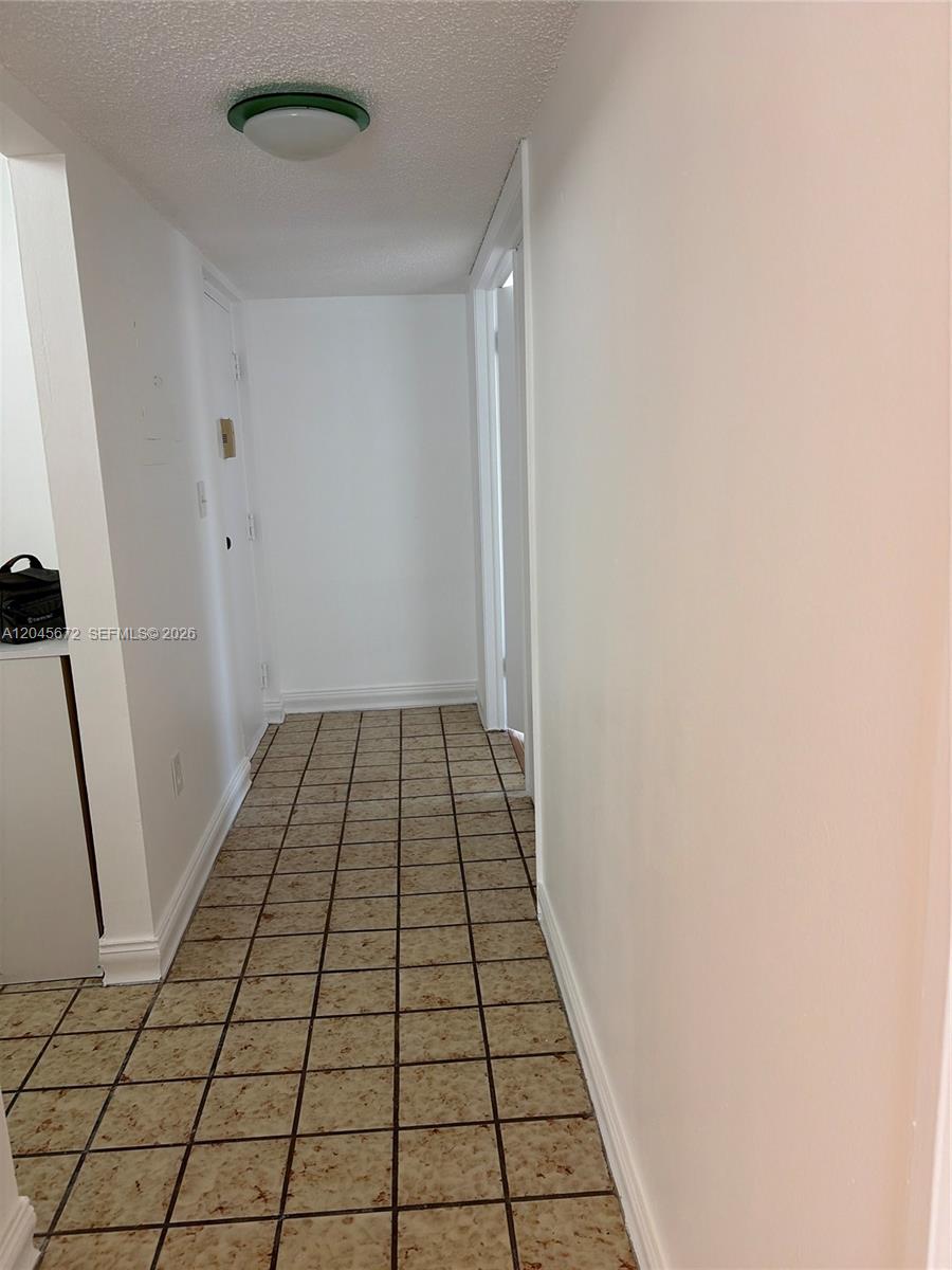 A narrow hallway features white walls, a textured ceiling, and square, speckled floor tiles — 1150 Collins Ave # 404, Miami Beach FL 33139, MIAMI BEACH, FL