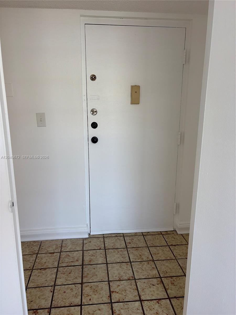 A white door with multiple locks and a light switch is set against a tiled floor — 1150 Collins Ave # 404, Miami Beach FL 33139, MIAMI BEACH, FL