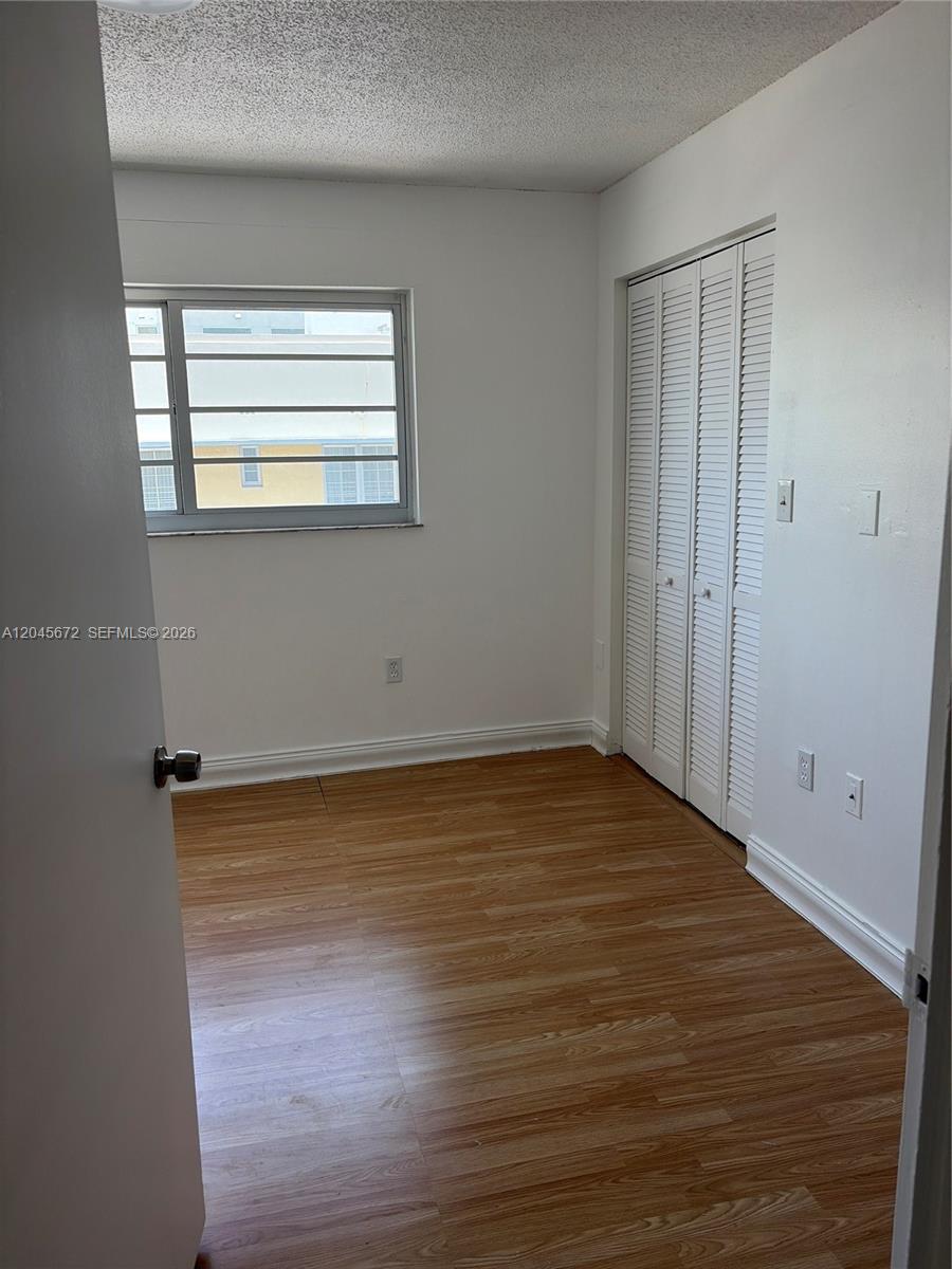 An empty bedroom features white walls, wood-look flooring, a window, and a white louvered closet — 1150 Collins Ave # 404, Miami Beach FL 33139, MIAMI BEACH, FL