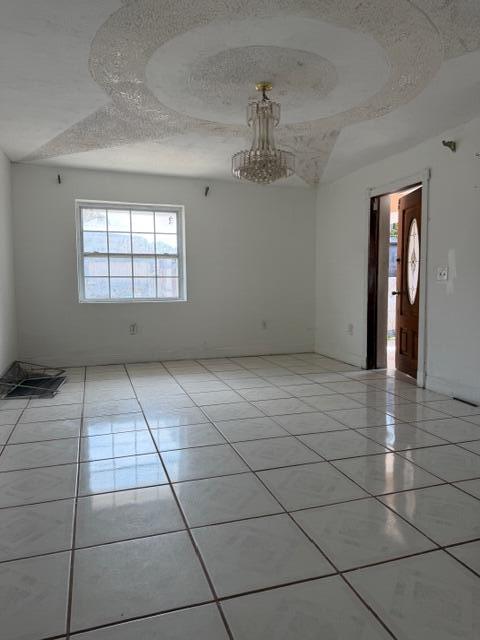 An empty room features white tiled floors, a textured ceiling medallion, and a crystal chandelier — 2975 NW 96th Street, Miami FL 33147, MIAMI, FL