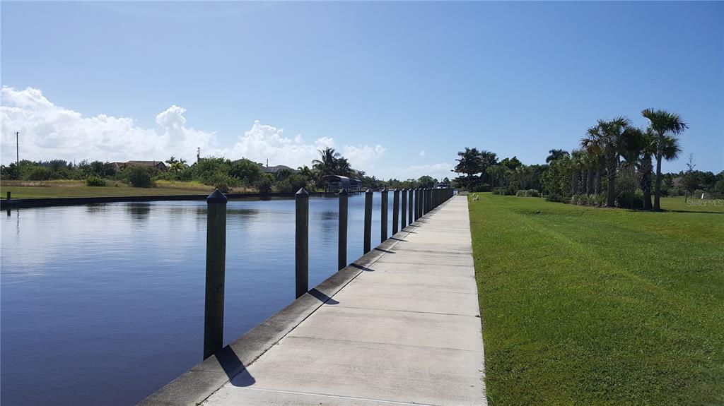 A concrete walkway runs alongside a canal lined with wooden pilings and grassy banks — 10022 CALUMET BOULEVARD, PORT CHARLOTTE, FL