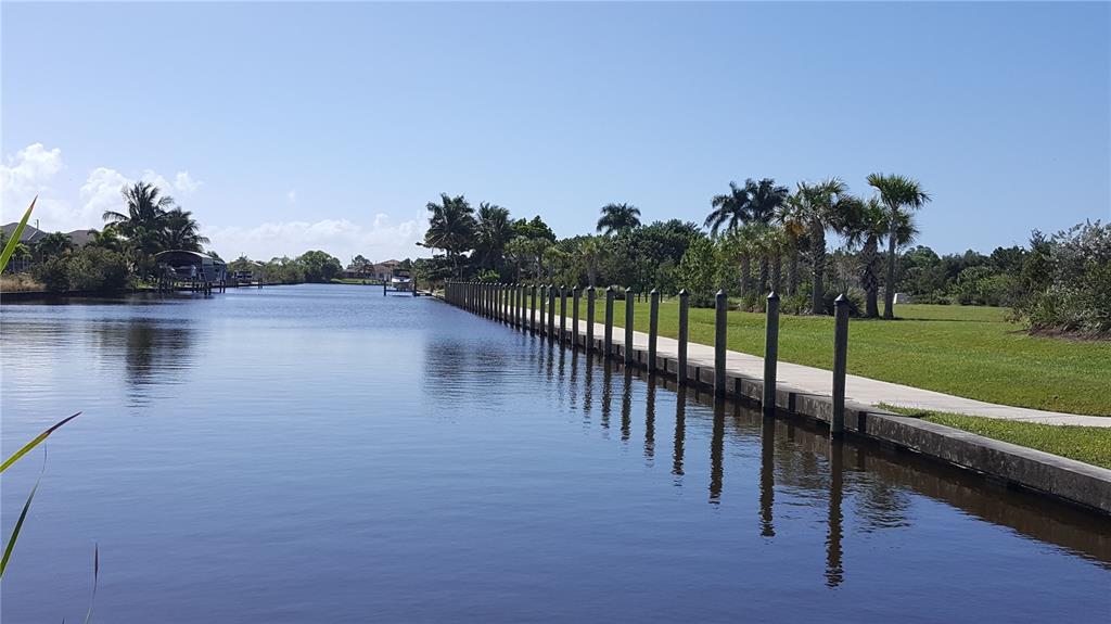 A canal view features a long concrete seawall with wooden pilings along a grassy bank — 10022 CALUMET BOULEVARD, PORT CHARLOTTE, FL