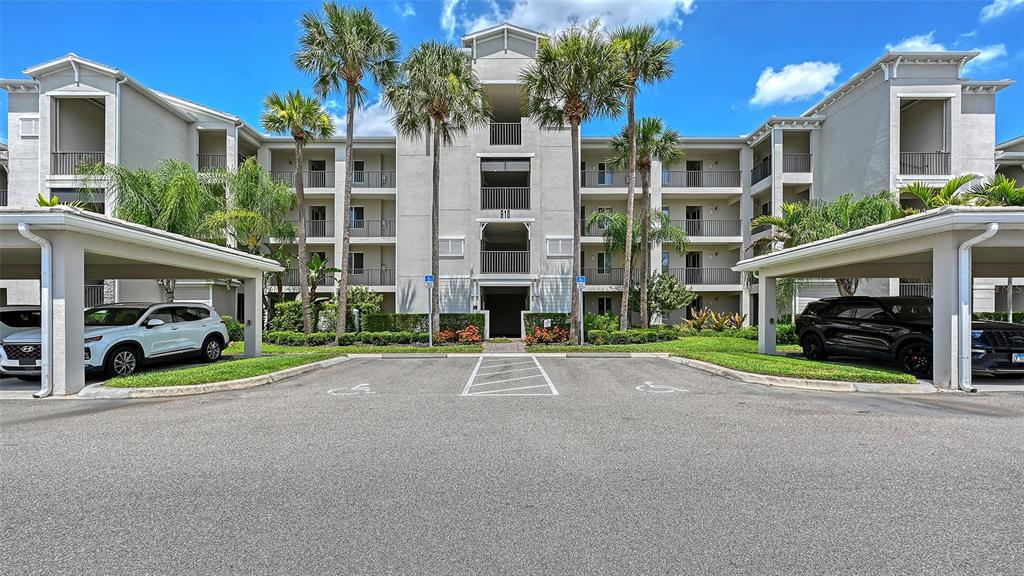 A multi-story apartment building with covered parking spaces and palm trees in the foreground — 910 TIDEWATER SHORES LOOP UNIT 103, BRADENTON, FL