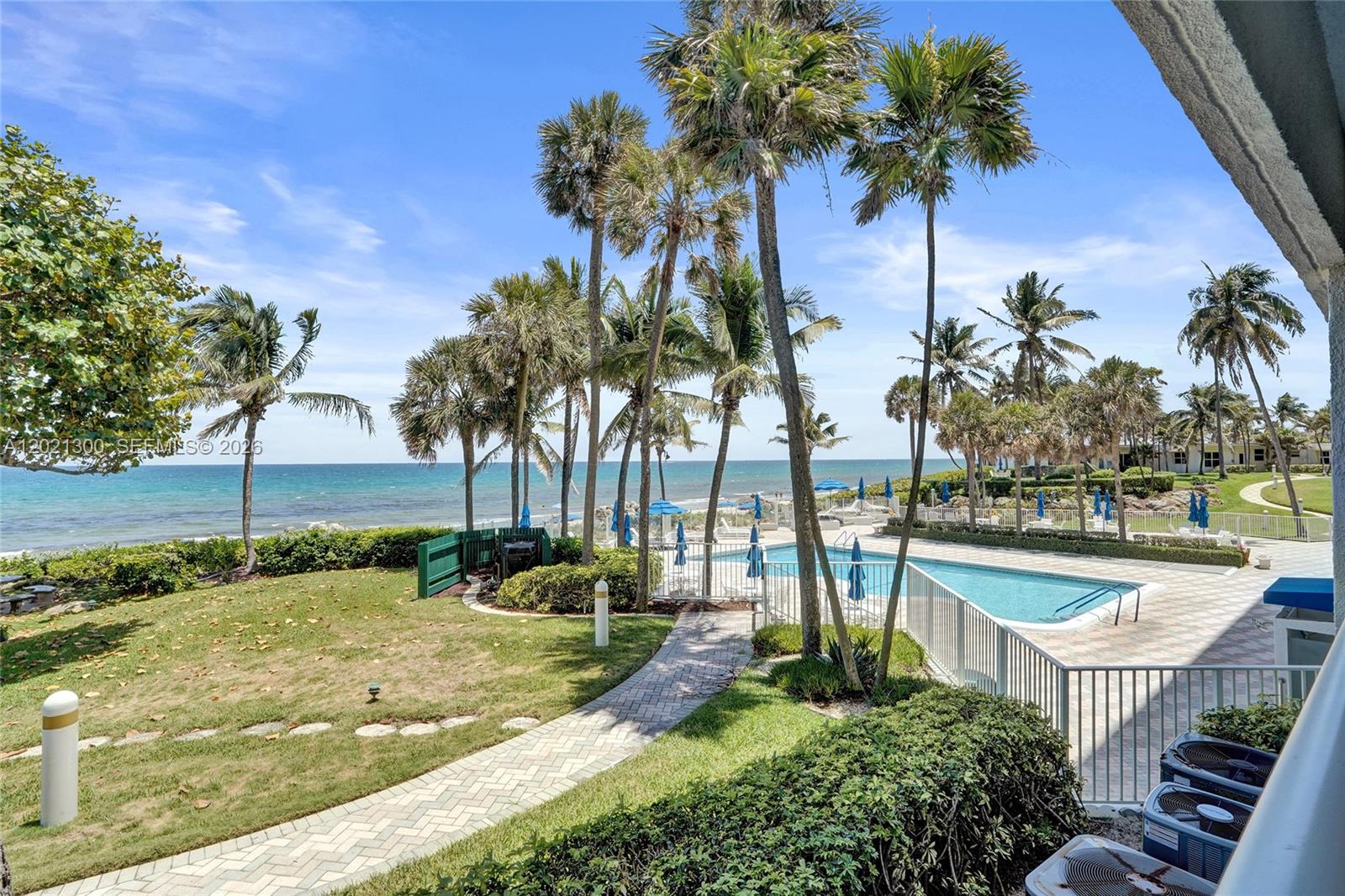 A view of a swimming pool, palm trees, and the ocean from a patio — 500 SE 21st Ave # 211, Deerfield Beach FL 33441, DEERFIELD BEACH, FL