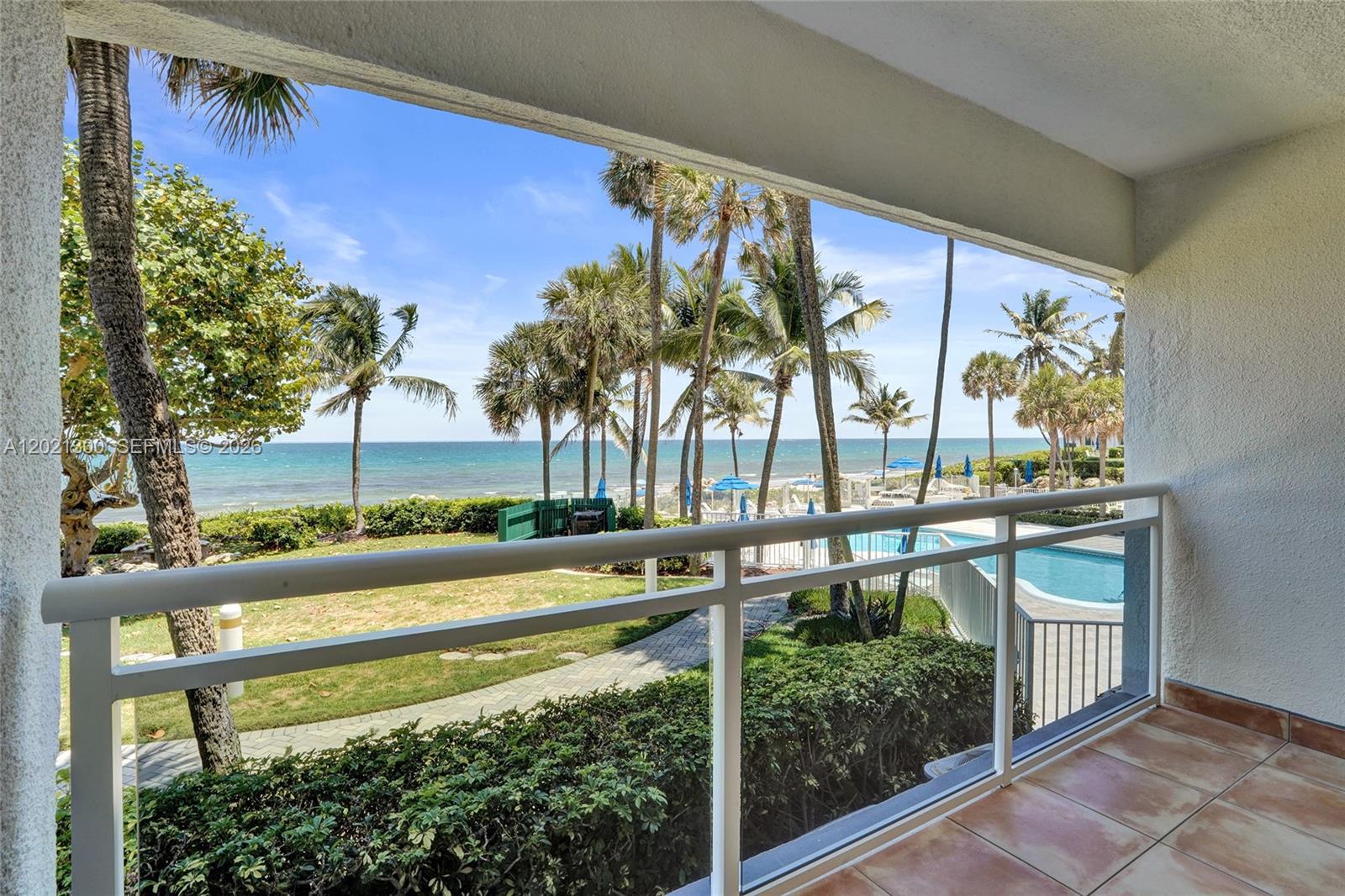 A balcony with a white railing overlooks a swimming pool, palm trees, and the ocean — 500 SE 21st Ave # 211, Deerfield Beach FL 33441, DEERFIELD BEACH, FL