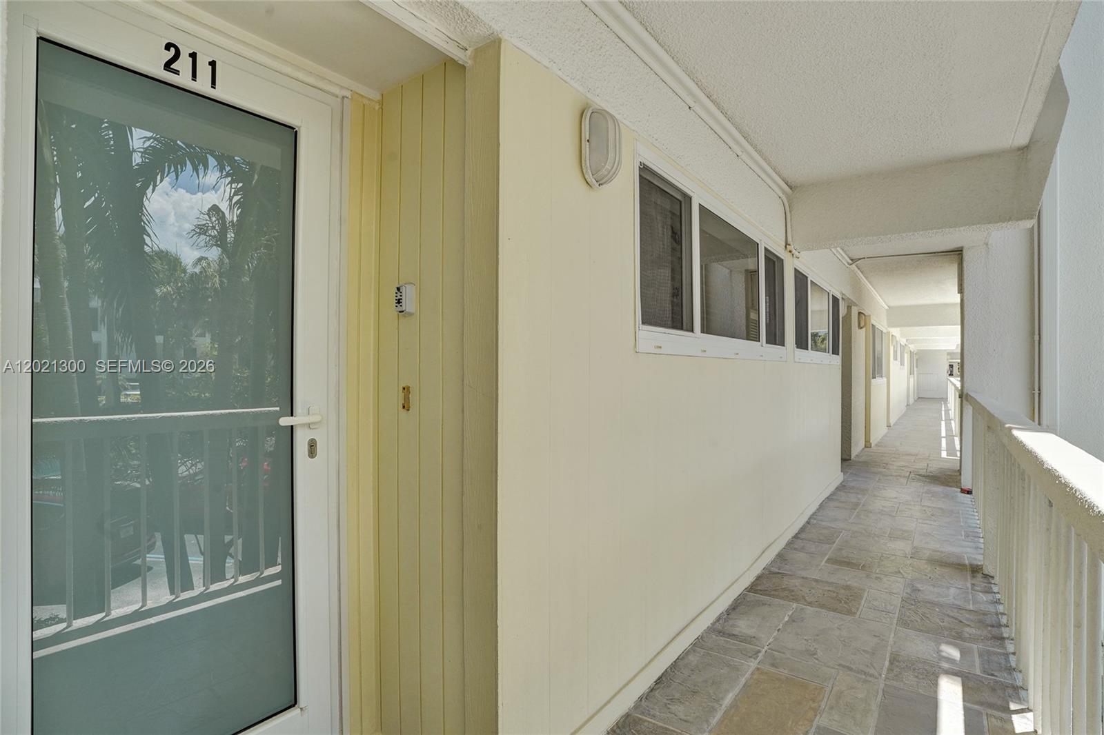 An exterior walkway leads to a residential unit door marked with the number 211 — 500 SE 21st Ave # 211, Deerfield Beach FL 33441, DEERFIELD BEACH, FL