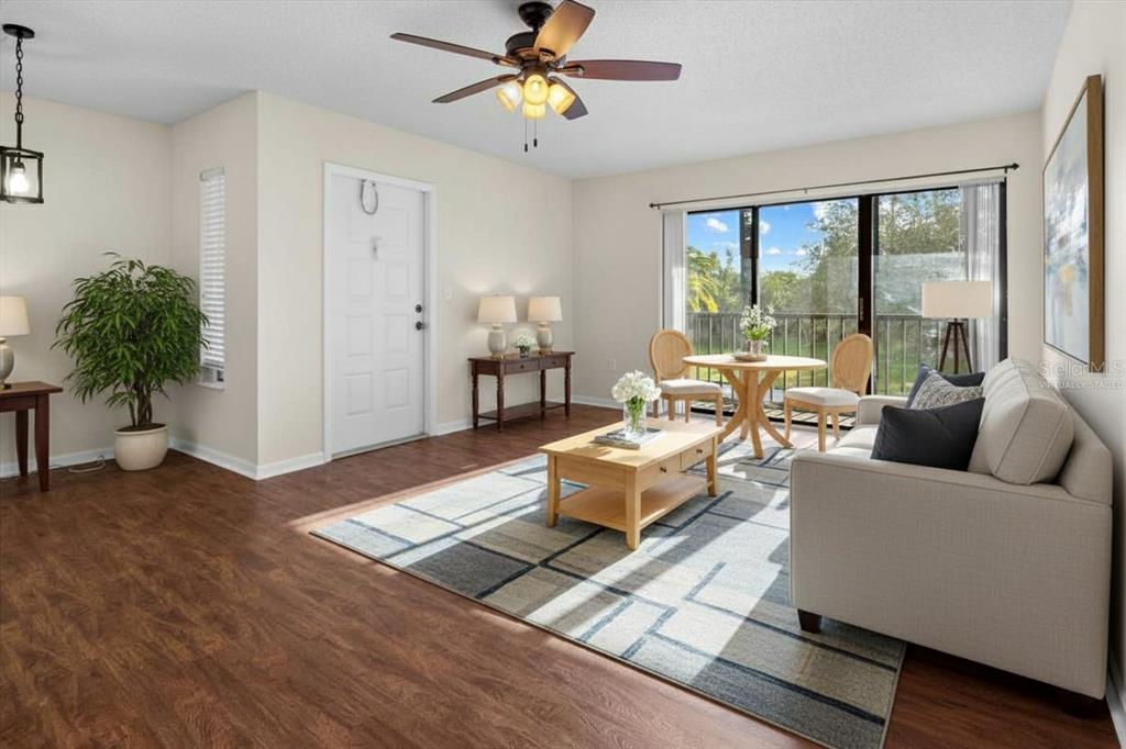 A living room with wood-look flooring, a ceiling fan, and a sliding glass balcony door — 1127 PINE RIDGE CIRCLE W UNIT A2, TARPON SPRINGS, FL