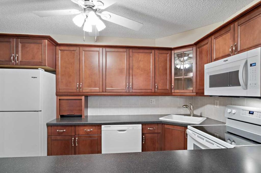 A kitchen features wood cabinets, white appliances, a dark countertop, and a ceiling fan — 1127 PINE RIDGE CIRCLE W UNIT A2, TARPON SPRINGS, FL