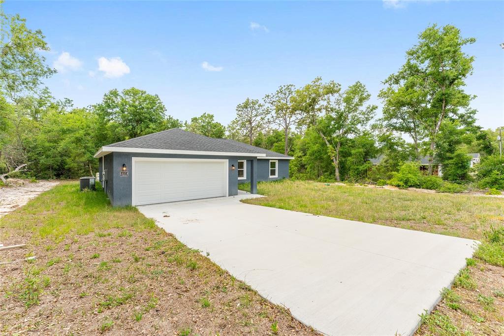 A gray single-story house with a white garage door and a concrete driveway — 10374 SE 126TH LANE, BELLEVIEW, FL