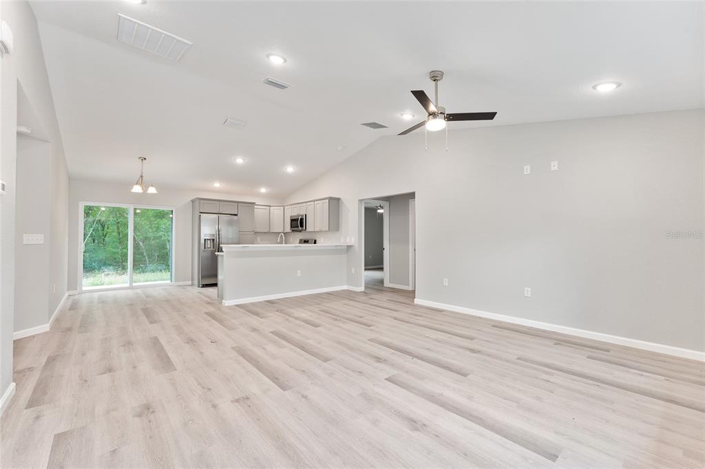 An open-concept living area features light wood-look flooring, a vaulted ceiling, and a kitchen island — 10374 SE 126TH LANE, BELLEVIEW, FL