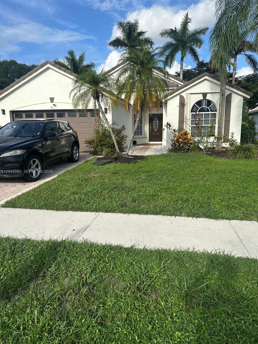 A single-story house with a tan stucco exterior, a two-car garage, and palm trees — 1971 Oak Berry Cir, Wellington FL 33414, WELLINGTON, FL