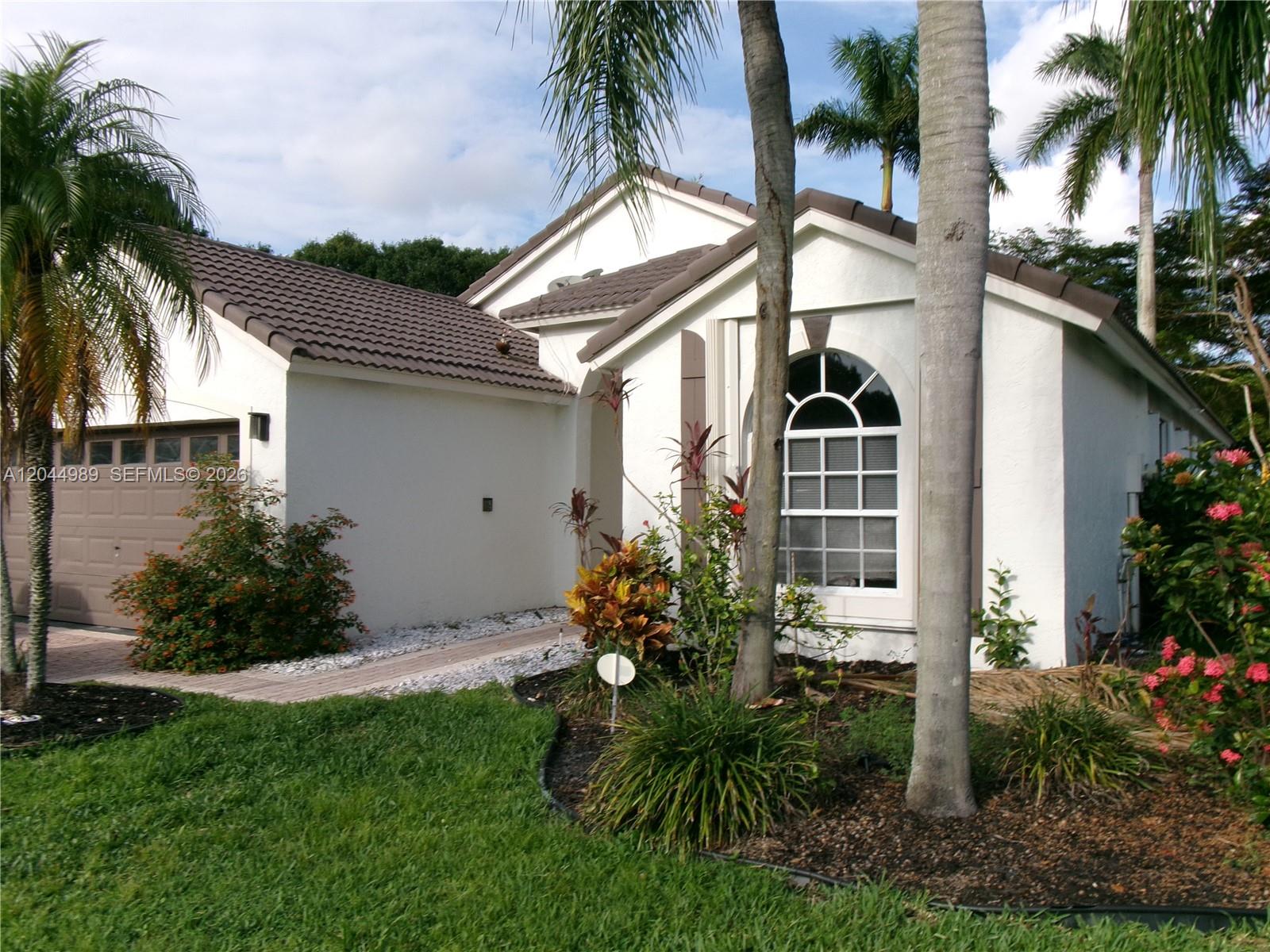 A single-story white house with a brown tile roof, garage, and palm trees in front — 1971 Oak Berry Cir, Wellington FL 33414, WELLINGTON, FL