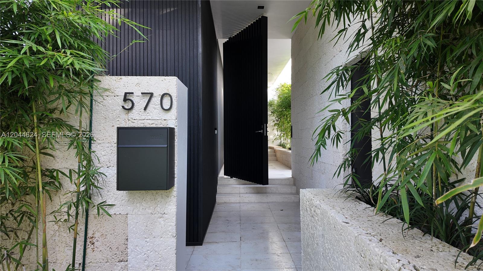 A modern entryway features a black door, stone walls, and bamboo plants — 570 S Shore Dr, Miami Beach FL 33141, MIAMI BEACH, FL