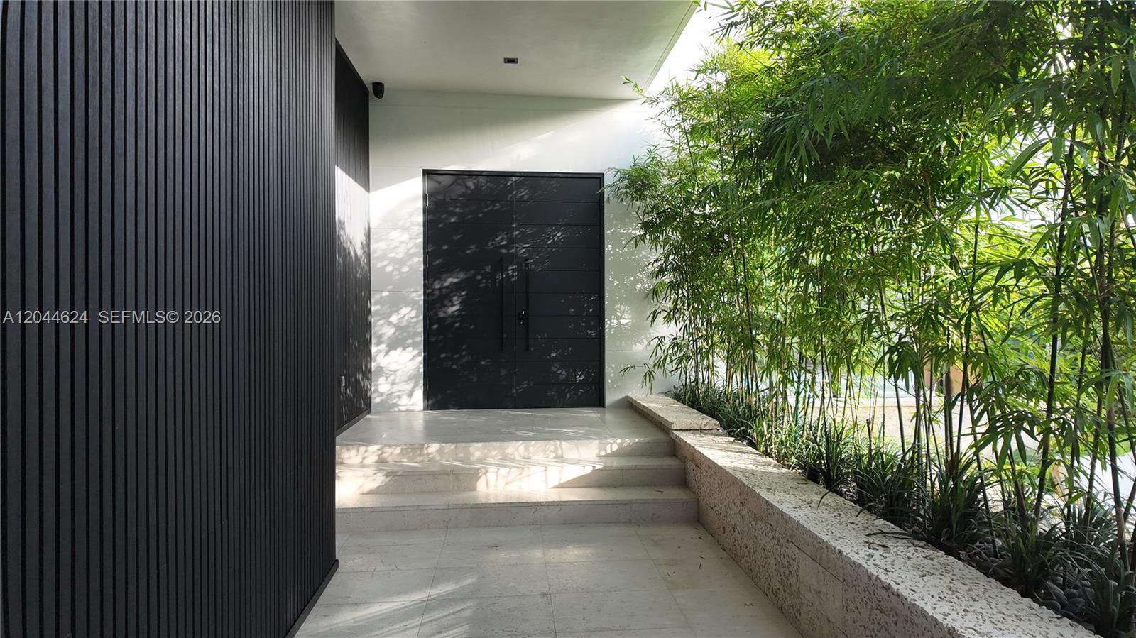A modern entryway features a black slatted wall, double doors, and stone steps beside bamboo — 570 S Shore Dr, Miami Beach FL 33141, MIAMI BEACH, FL