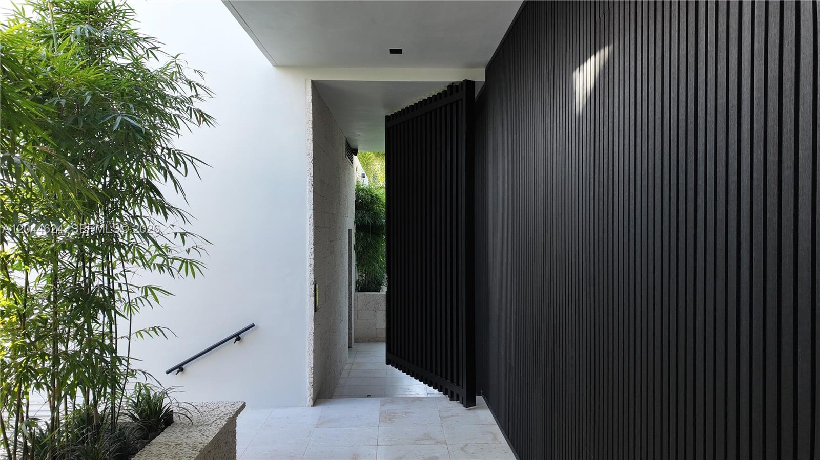 A modern entryway features a large, slatted black pivot door and white walls — 570 S Shore Dr, Miami Beach FL 33141, MIAMI BEACH, FL