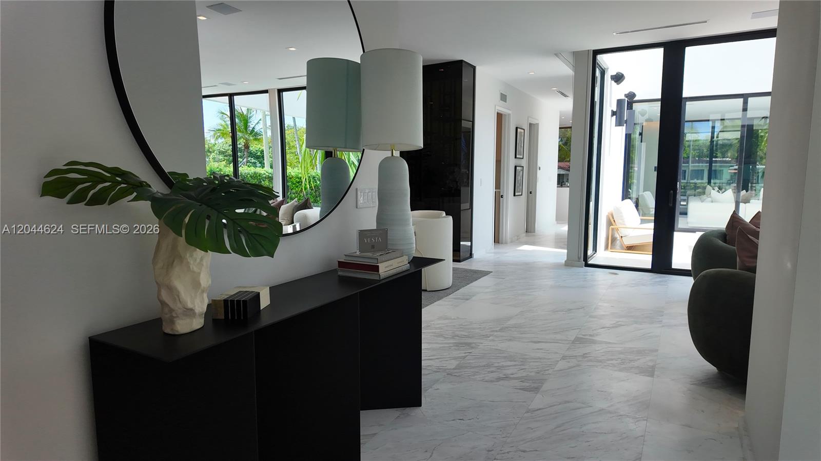 A modern entryway features a black console table, a large round mirror, and marble flooring — 570 S Shore Dr, Miami Beach FL 33141, MIAMI BEACH, FL