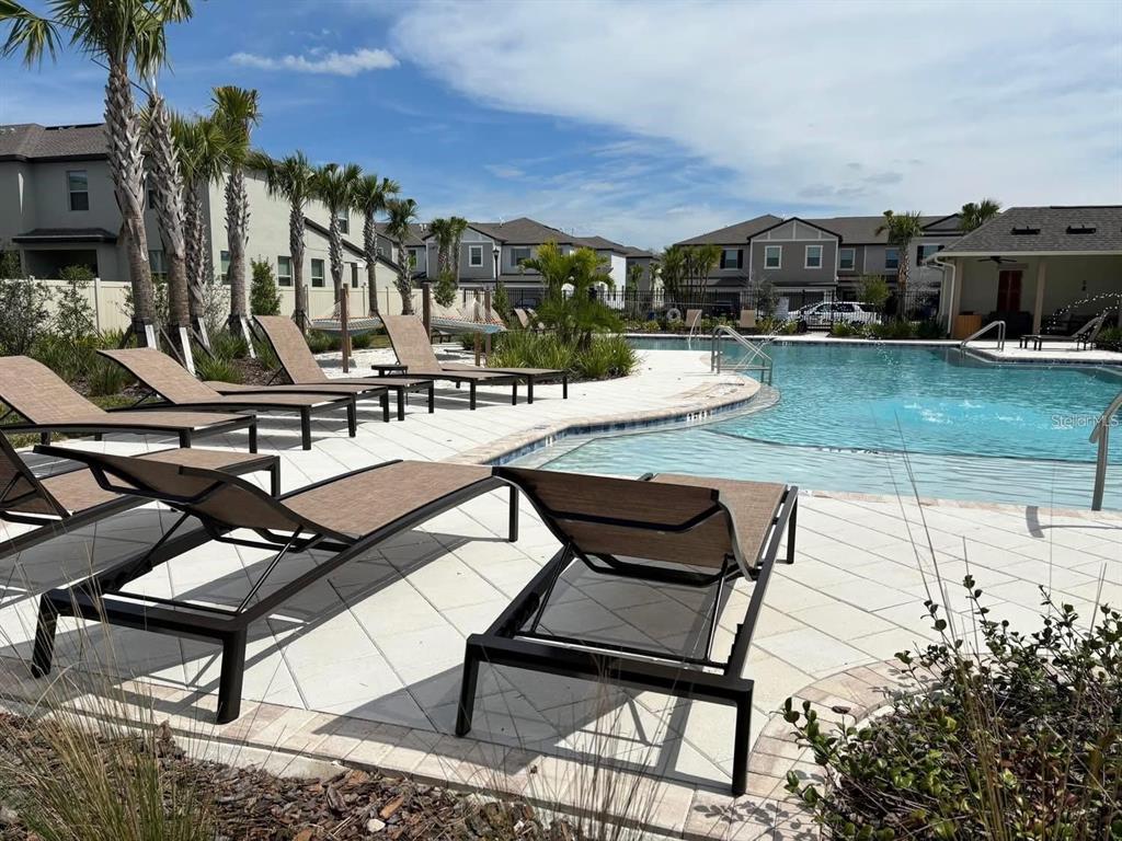 A swimming pool with lounge chairs on a paved deck surrounded by residential buildings — 8254 CORNER PINE WAY, NEW PORT RICHEY, FL