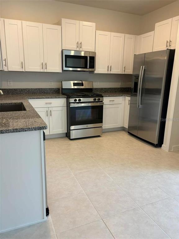 A kitchen features white cabinets, stainless steel appliances, and gray granite countertops — 8254 CORNER PINE WAY, NEW PORT RICHEY, FL