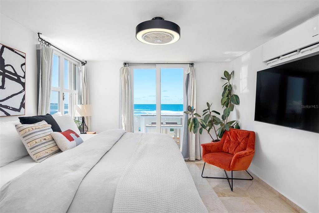 A bedroom features a large bed, an orange armchair, and a balcony overlooking the ocean — Villas de COSTA DORADA UNIT H3, DORADO, PR