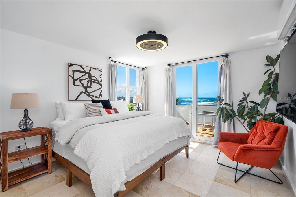 A bedroom features a bed, an orange chair, and a balcony overlooking the ocean — Villas de COSTA DORADA UNIT H3, DORADO, PR