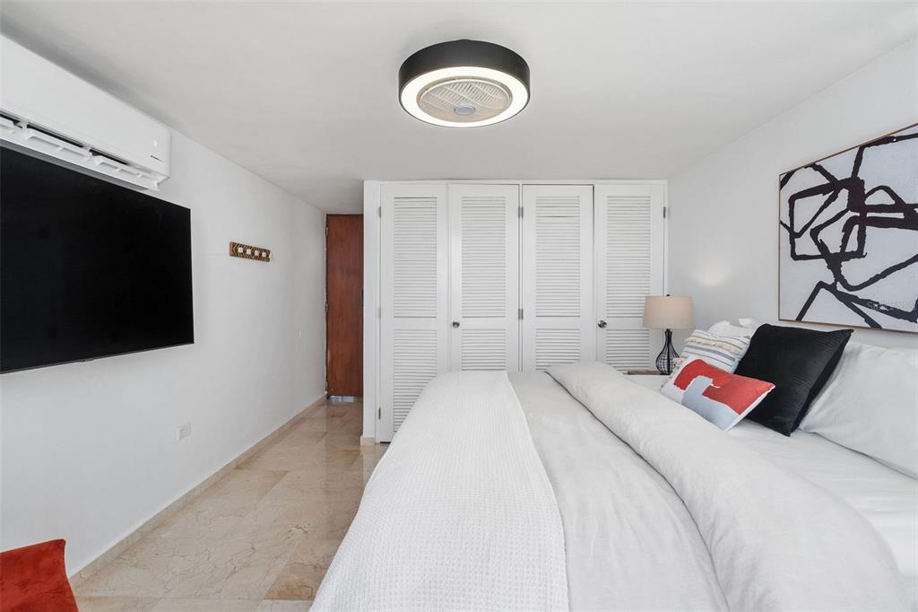 A bedroom features a large bed, a wall-mounted television, and a ceiling fan light fixture — Villas de COSTA DORADA UNIT H3, DORADO, PR
