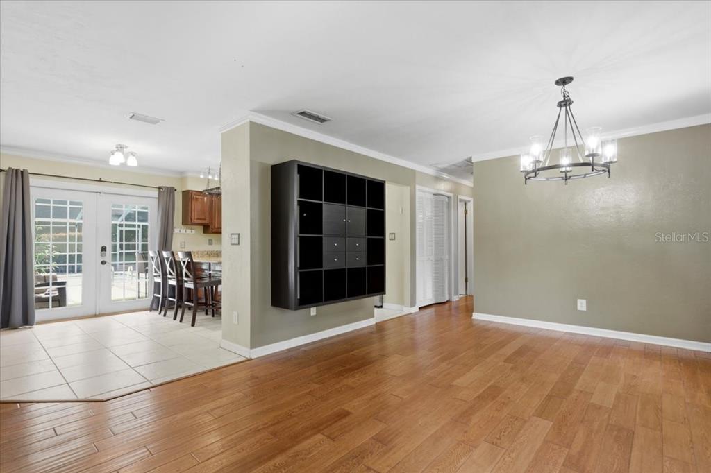An open living area features hardwood floors, a wall-mounted black shelving unit, and a chandelier — 5515 SW 35TH WAY, GAINESVILLE, FL