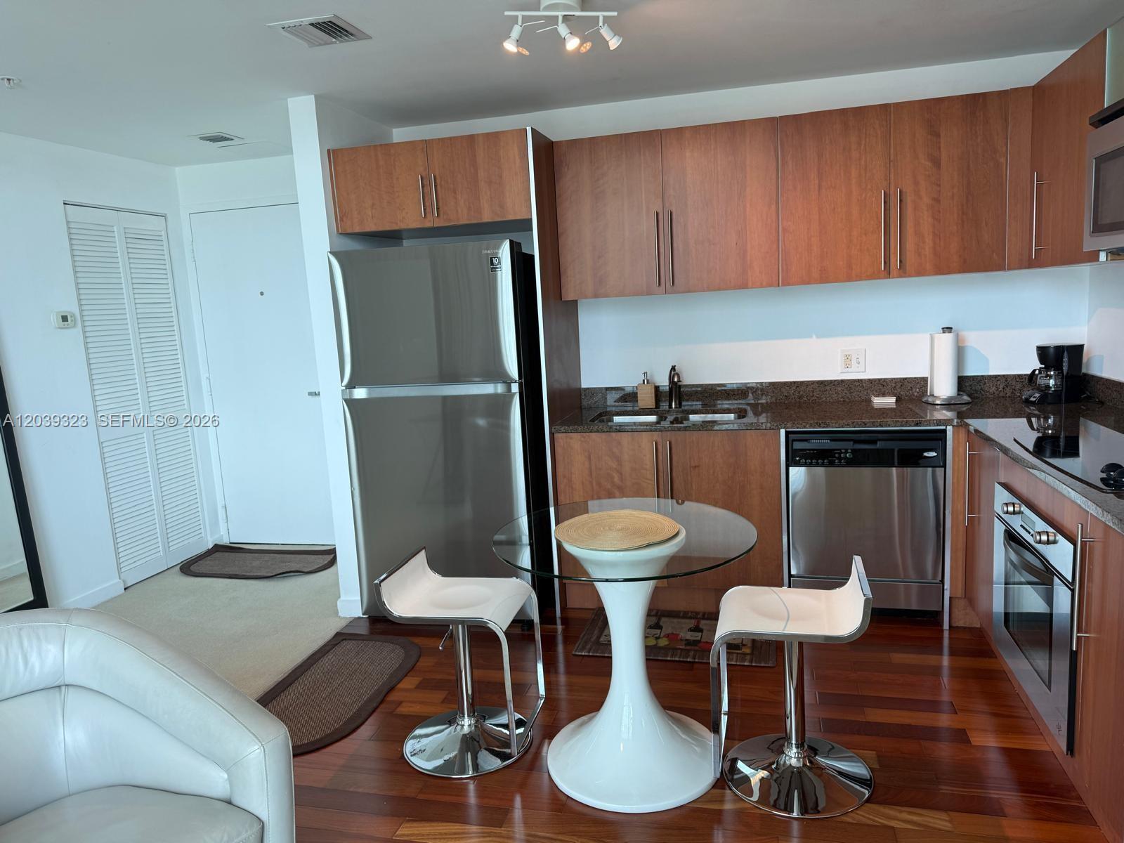 A kitchen features wood cabinets, stainless steel appliances, a glass table, and two white stools — 300 S Biscayne Blvd # 3703, Miami FL 33131, MIAMI, FL