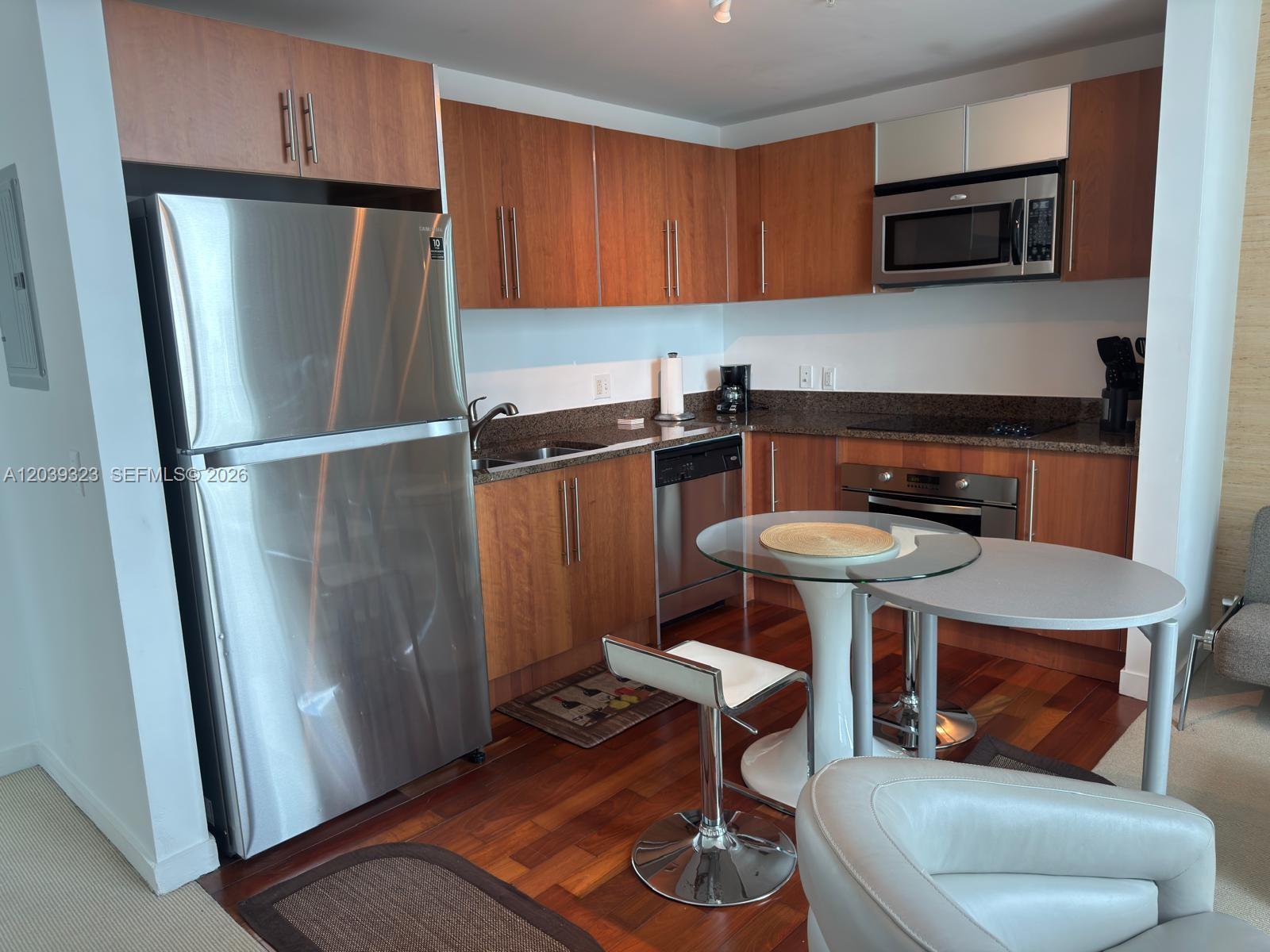 A kitchen features wood cabinets, stainless steel appliances, granite countertops, and a glass dining table — 300 S Biscayne Blvd # 3703, Miami FL 33131, MIAMI, FL