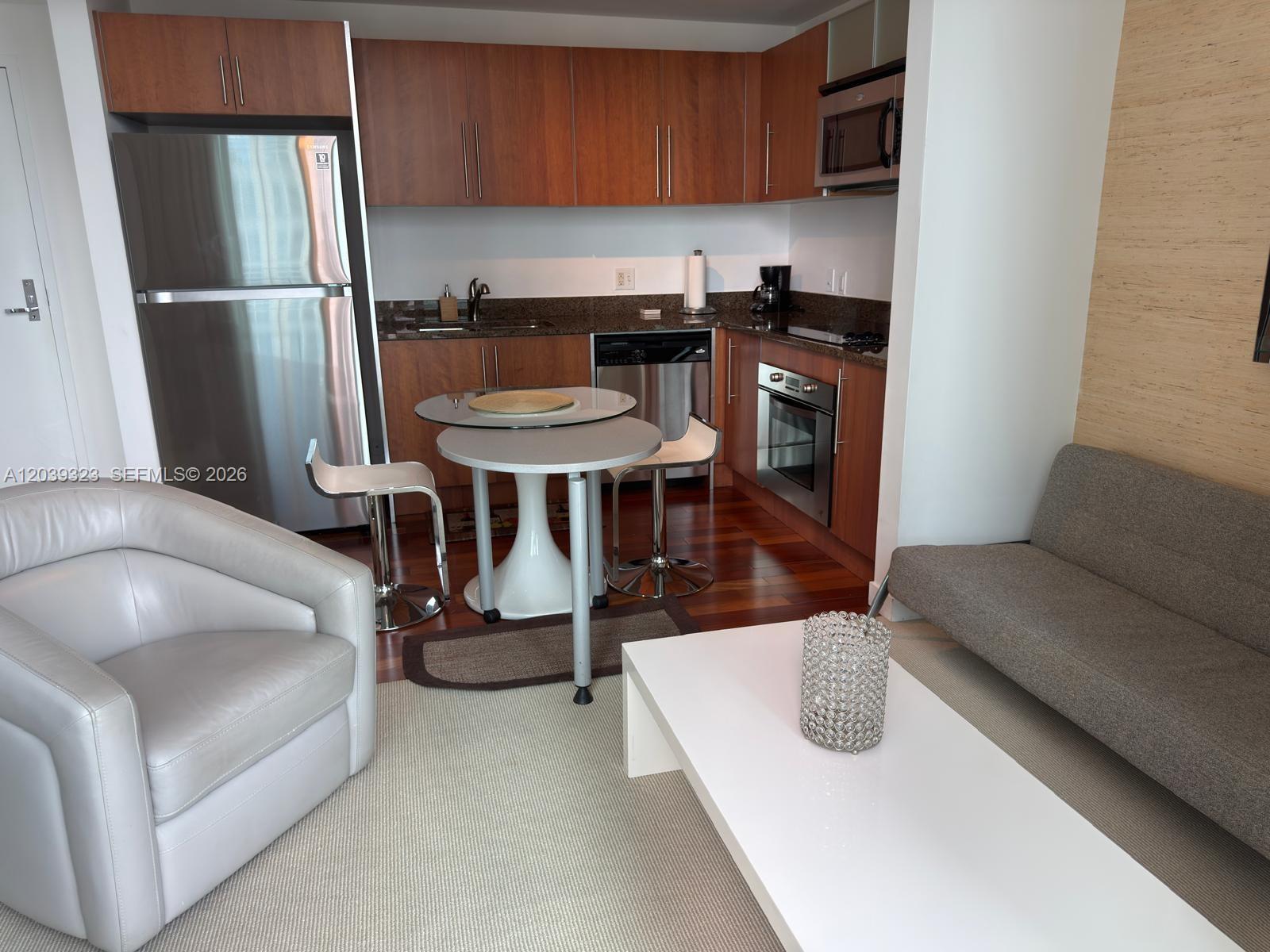 A small kitchen with wood cabinets and stainless steel appliances sits beside a living area — 300 S Biscayne Blvd # 3703, Miami FL 33131, MIAMI, FL