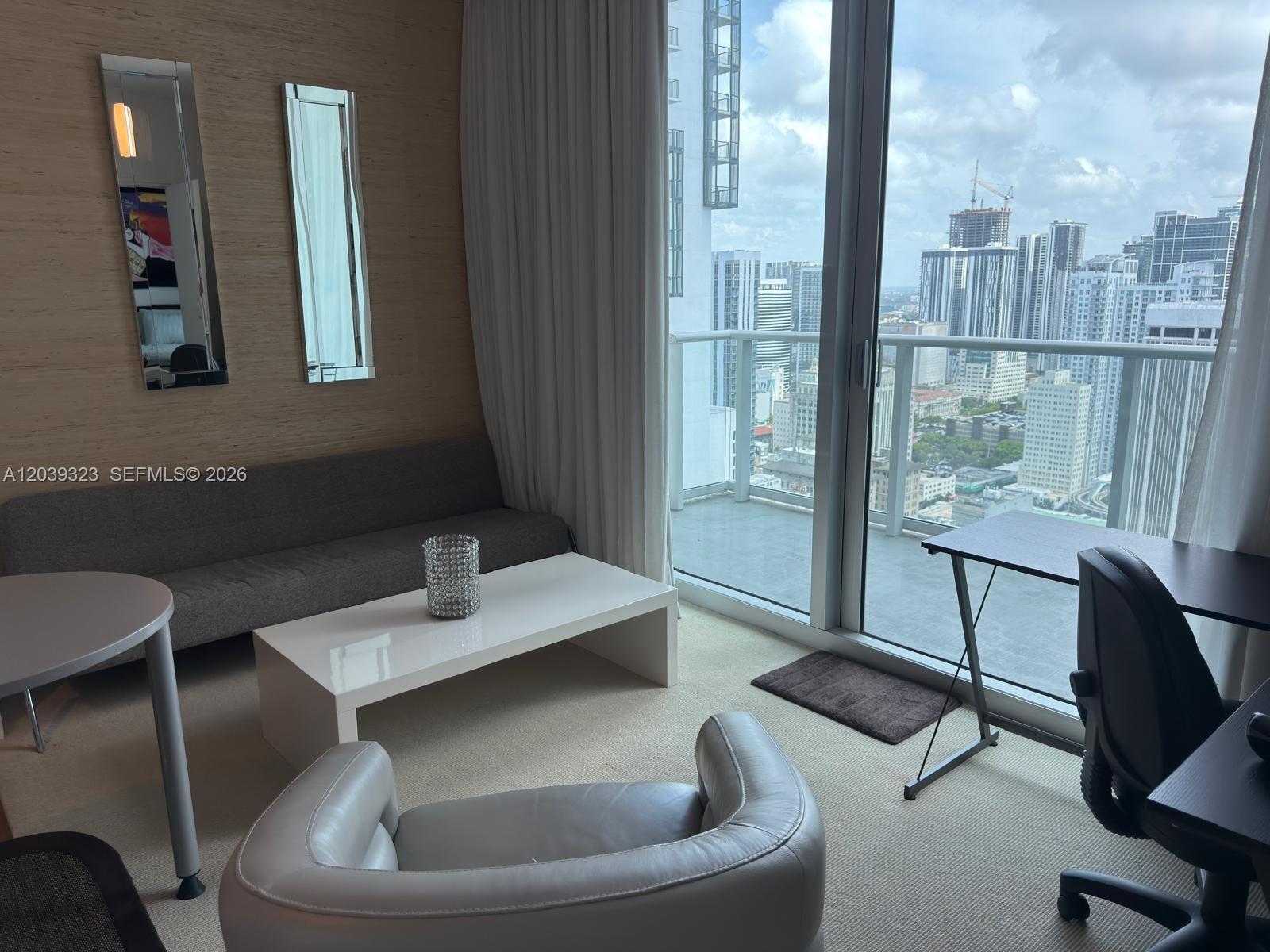A living room features a gray sofa, white coffee table, and balcony with city views — 300 S Biscayne Blvd # 3703, Miami FL 33131, MIAMI, FL